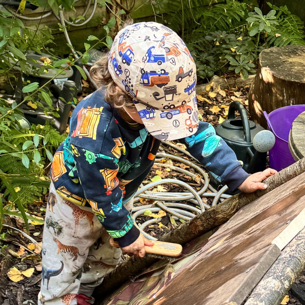 Child playing outdoors at nursery with wood object surrounded by nature